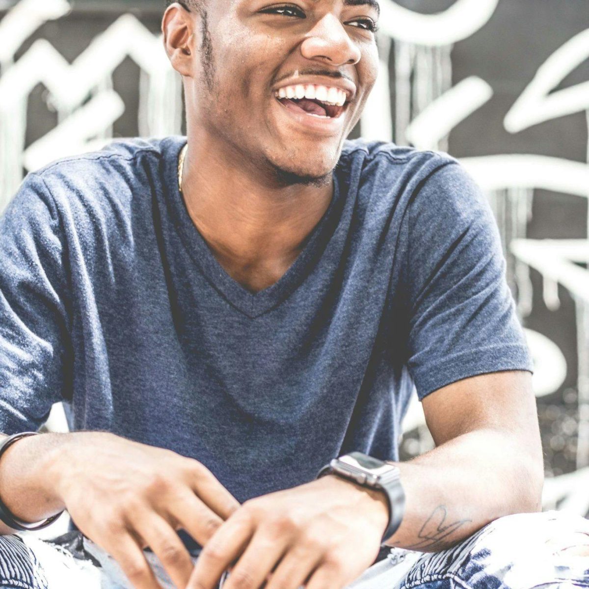 Young man laughing outdoors with a relaxed, natural smile in casual clothing