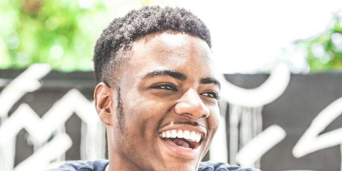 Young man laughing outdoors with a relaxed, natural smile in casual clothing