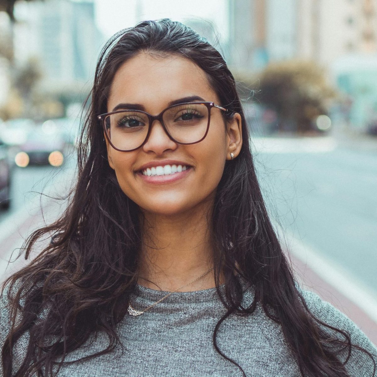 Woman with glasses smiling confidently on a city street, captured in natural daylight
