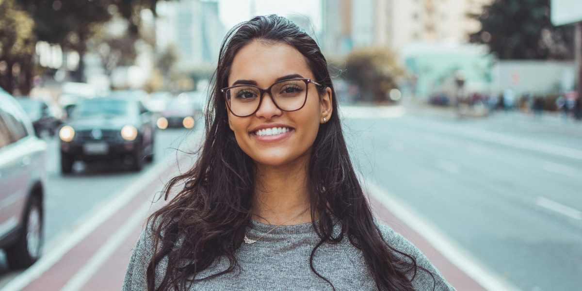 Woman with glasses smiling confidently on a city street, captured in natural daylight