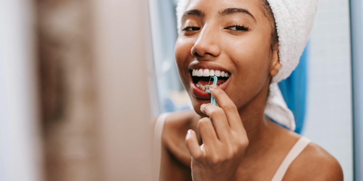 Woman flossing her teeth while smiling in a bathroom mirror after getting ready
