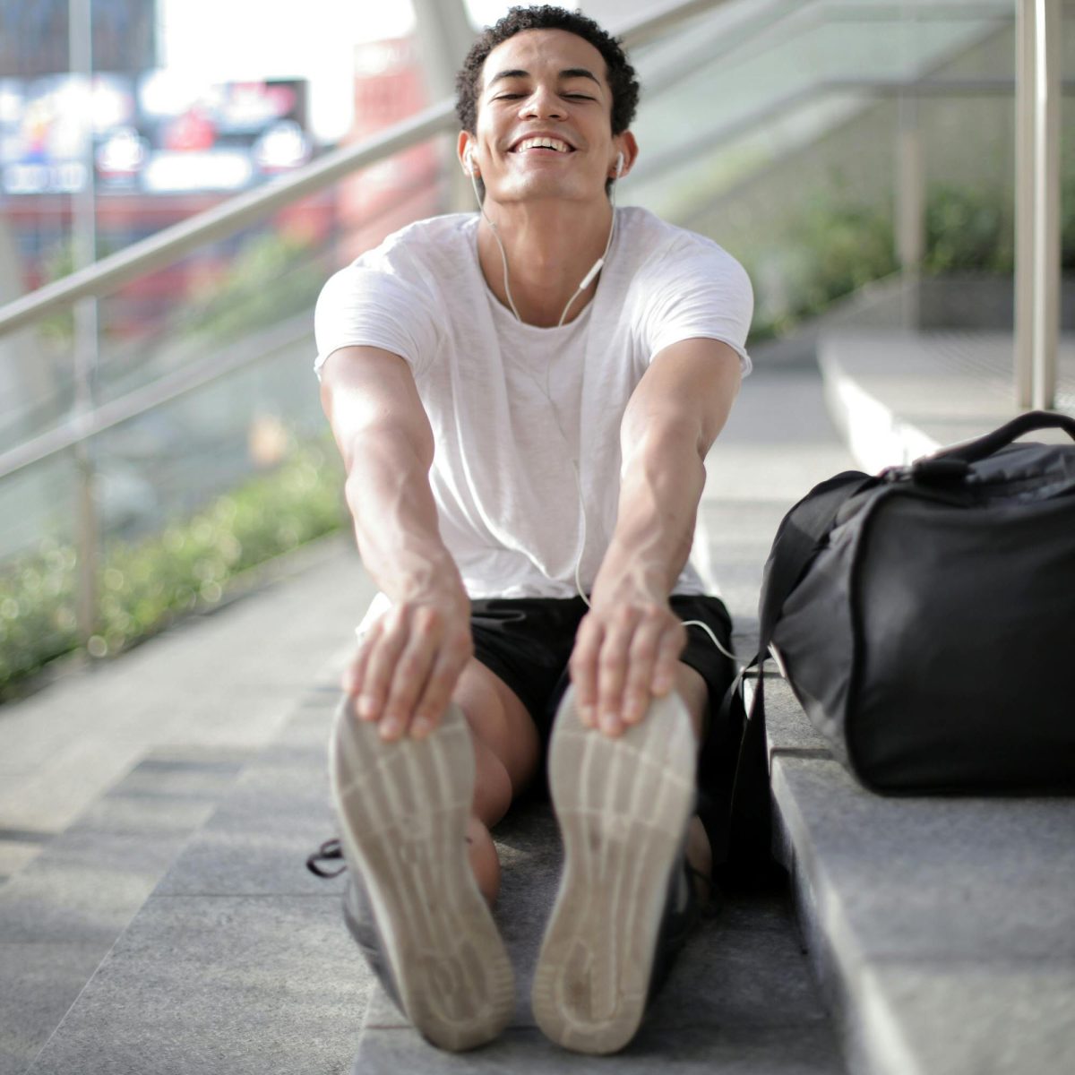 Young man stretching on outdoor steps, smiling comfortably during a casual workout break