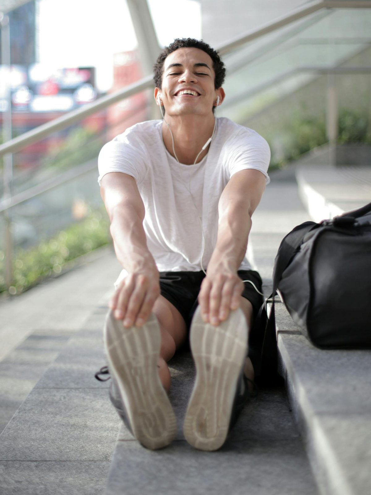 Young man stretching on outdoor steps, smiling comfortably during a casual workout break
