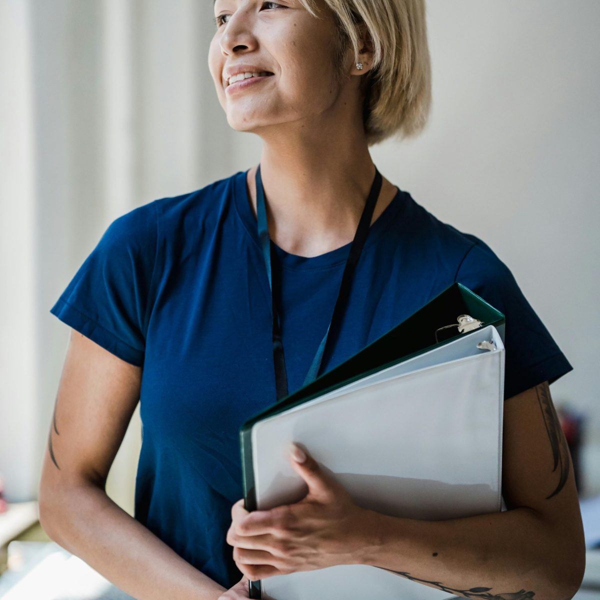 Woman holding a folder and smiling softly while looking out a window in a professional setting