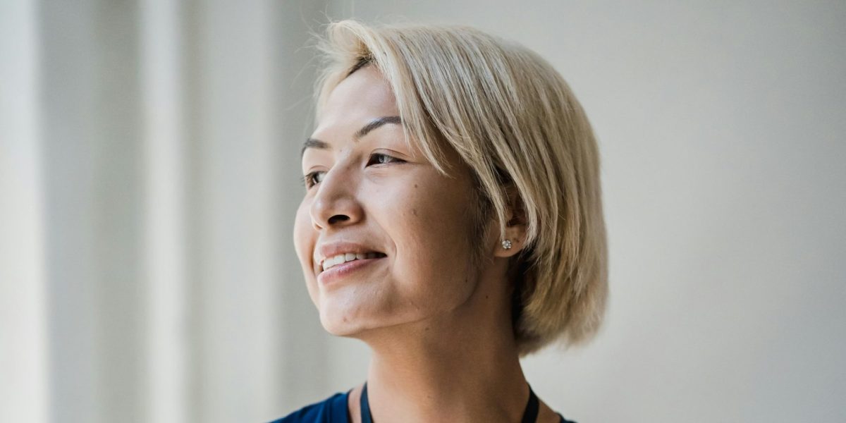 Woman holding a folder and smiling softly while looking out a window in a professional setting