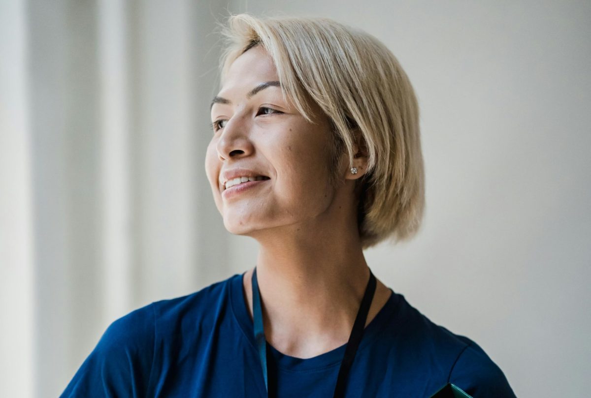 Woman holding a folder and smiling softly while looking out a window in a professional setting