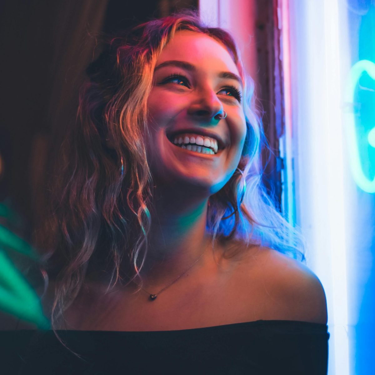 Woman smiling naturally in colorful neon light, captured in a candid nighttime portrait