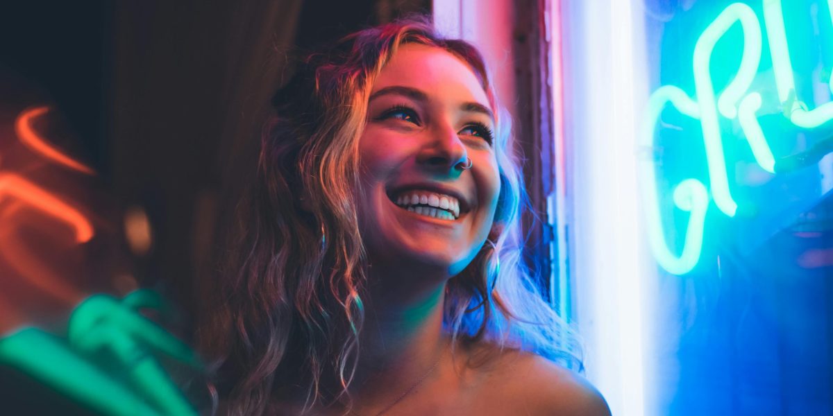 Woman smiling naturally in colorful neon light, captured in a candid nighttime portrait