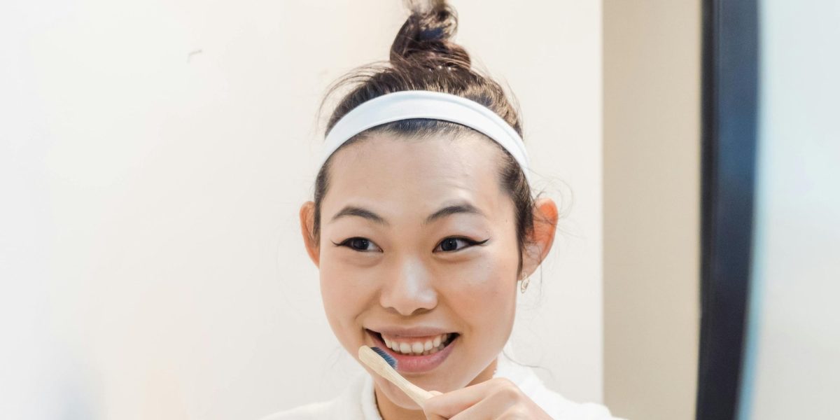 Woman in a robe brushing her teeth while smiling at her reflection in a bathroom mirror