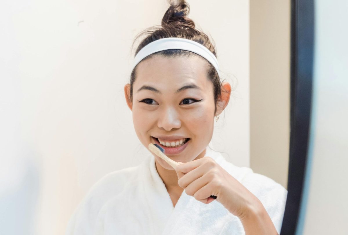 Woman in a robe brushing her teeth while smiling at her reflection in a bathroom mirror