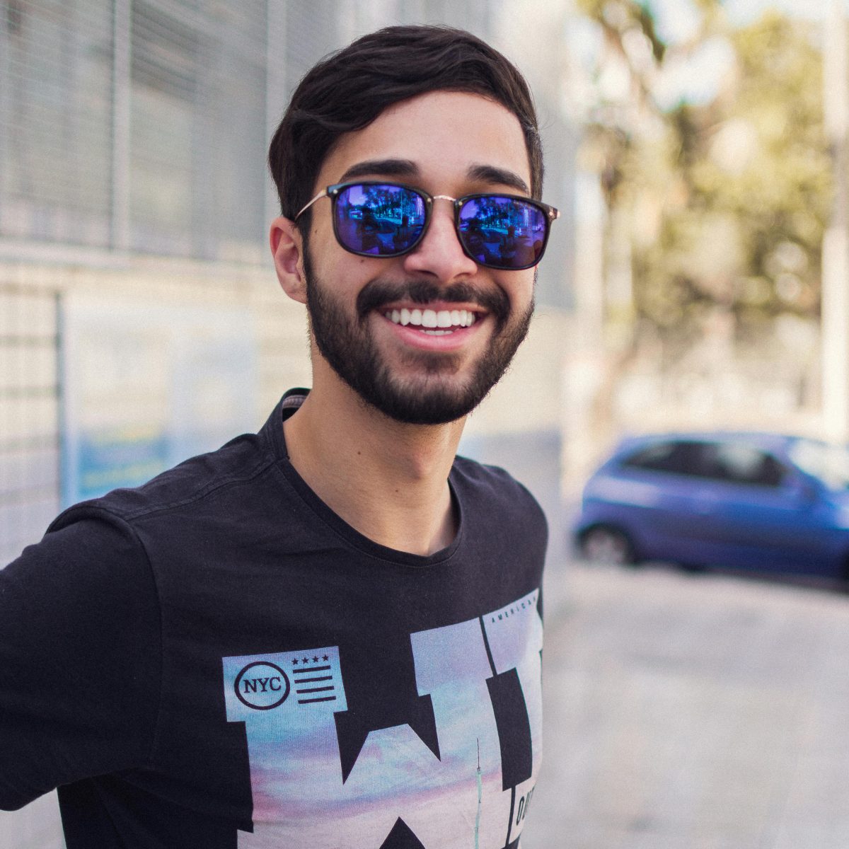 Man wearing sunglasses smiling casually outdoors on a city sidewalk