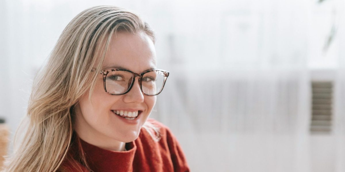Woman wearing glasses smiling while reading a book in a cozy indoor setting