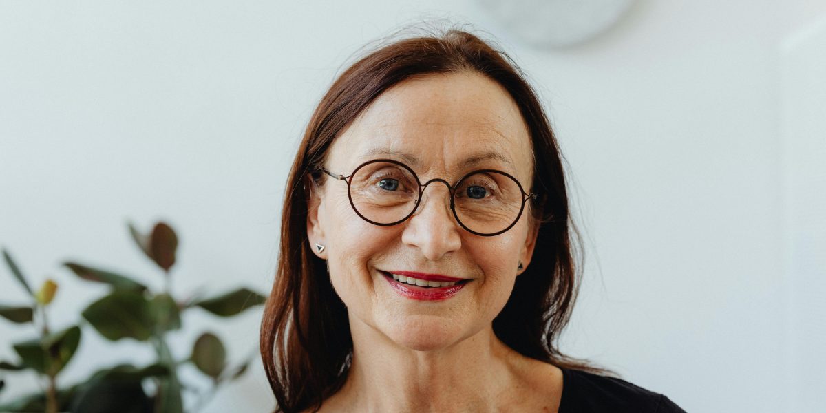 Older woman wearing glasses and smiling gently indoors, captured in soft natural light