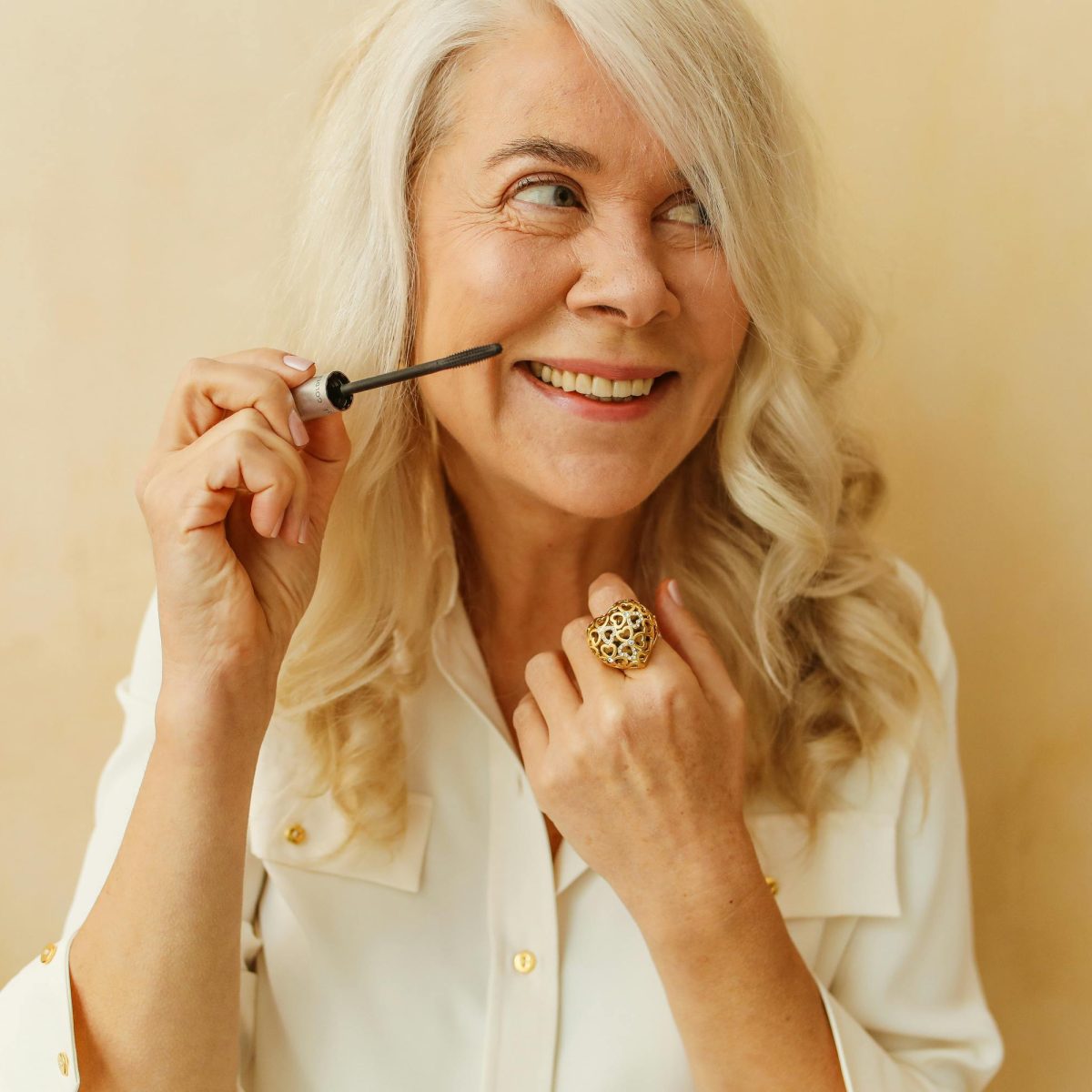 Older woman smiling naturally while applying makeup, showing healthy teeth and relaxed confidence