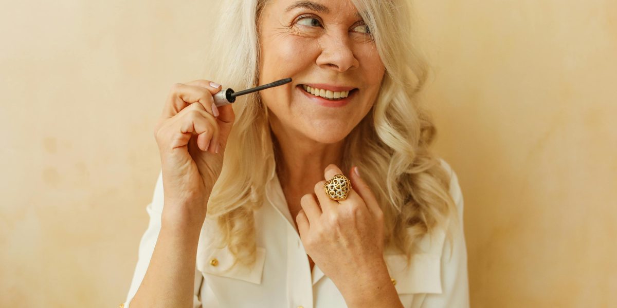 Older woman smiling naturally while applying makeup, showing healthy teeth and relaxed confidence