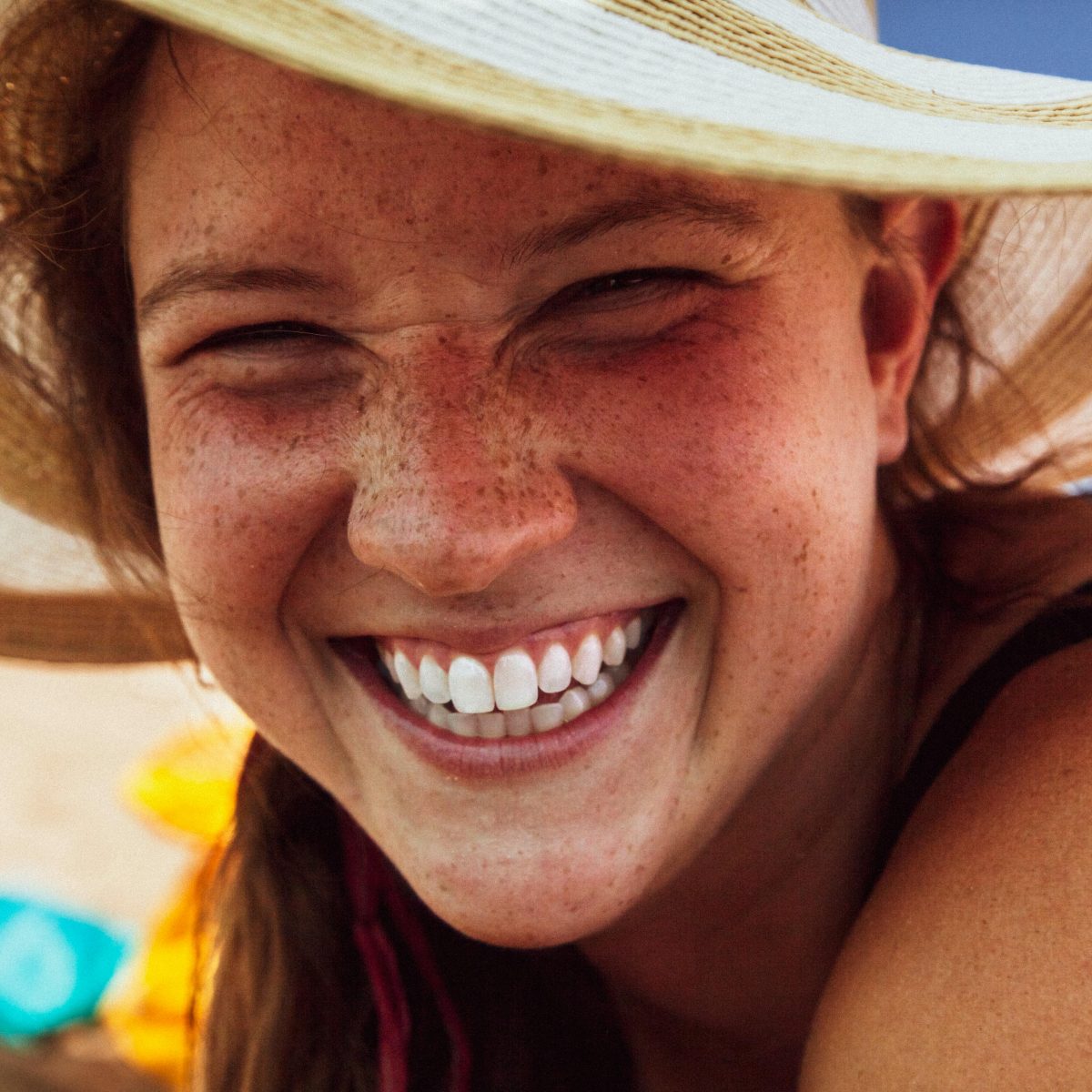 Woman wearing a sun hat smiling broadly outdoors, showing natural teeth and freckles